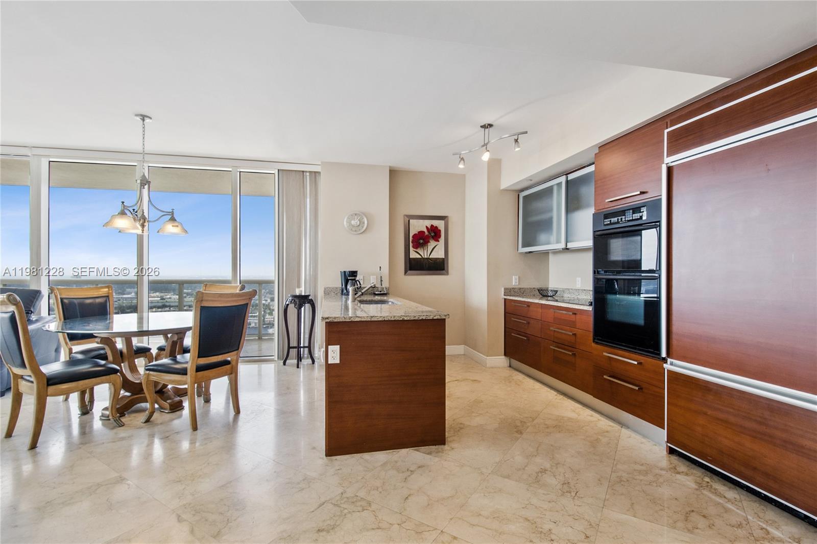 A modern kitchen features wood cabinetry, granite countertops, and a dining area with balcony views — 1830 S Ocean Dr # 4606, Hallandale Beach FL 33009, HALLANDALE BEACH, FL