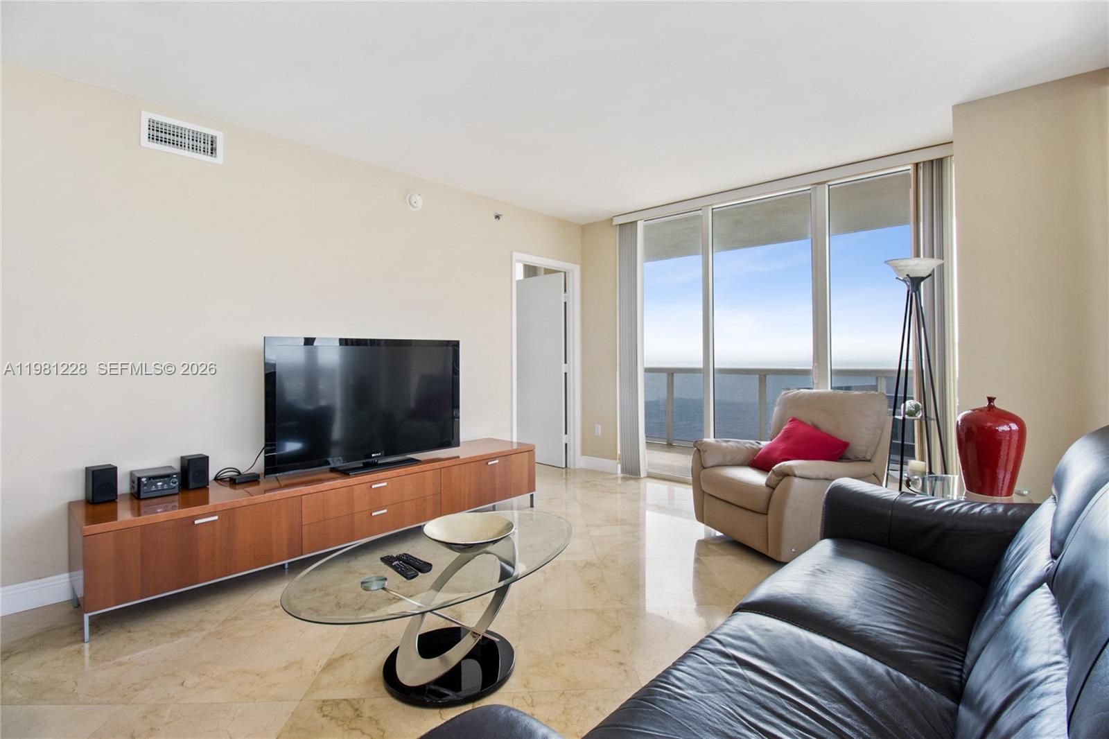 A living room features a television console, glass coffee table, leather sofa, and ocean views — 1830 S Ocean Dr # 4606, Hallandale Beach FL 33009, HALLANDALE BEACH, FL