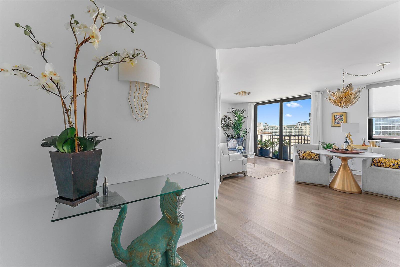 A bright living area features light wood floors, a glass console table, and balcony views — 651 Okeechobee Boulevard # 612, West Palm Beach FL 33401, WEST PALM BEACH, FL