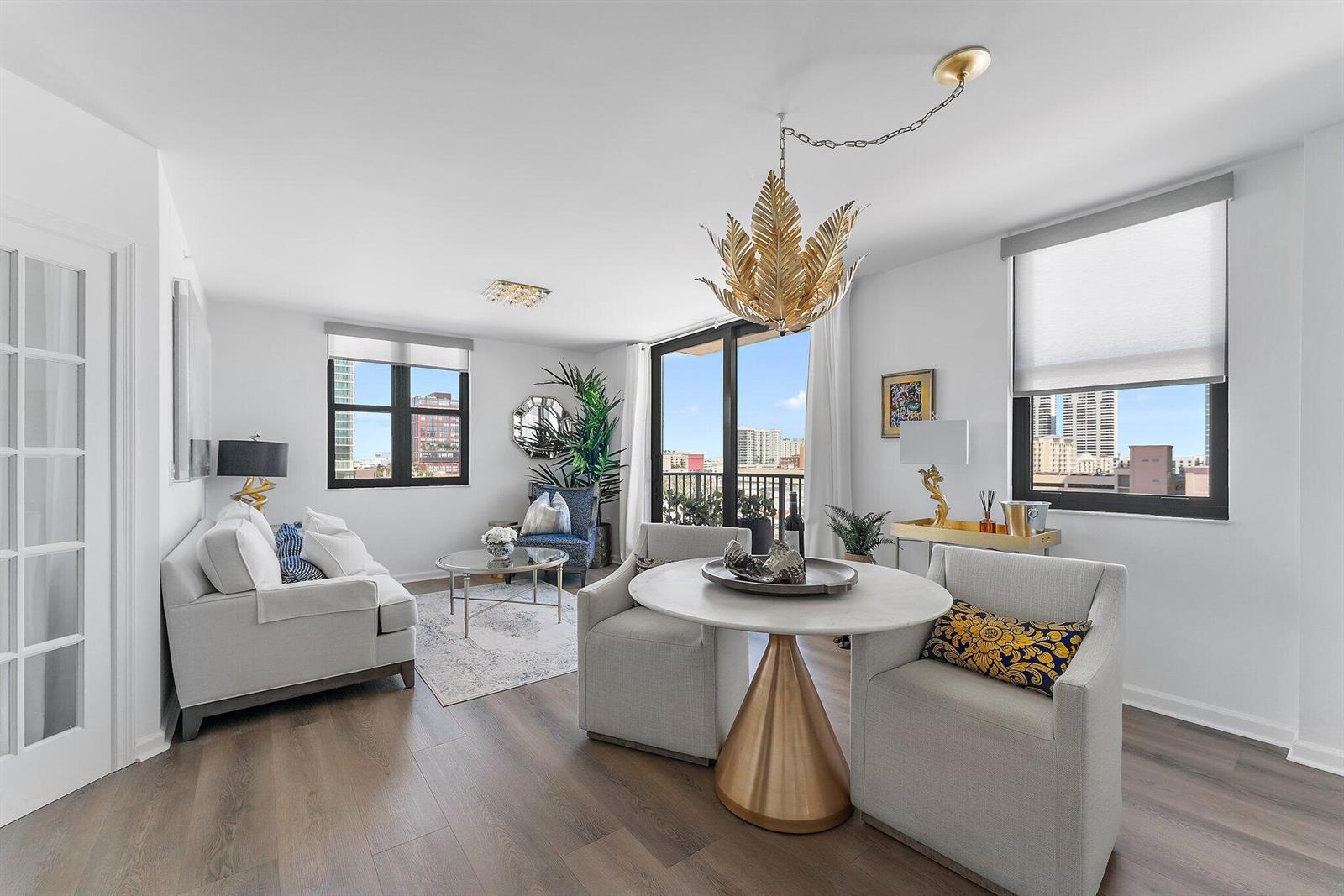 A living and dining area features light wood floors, a gold leaf chandelier, and city views — 651 Okeechobee Boulevard # 612, West Palm Beach FL 33401, WEST PALM BEACH, FL