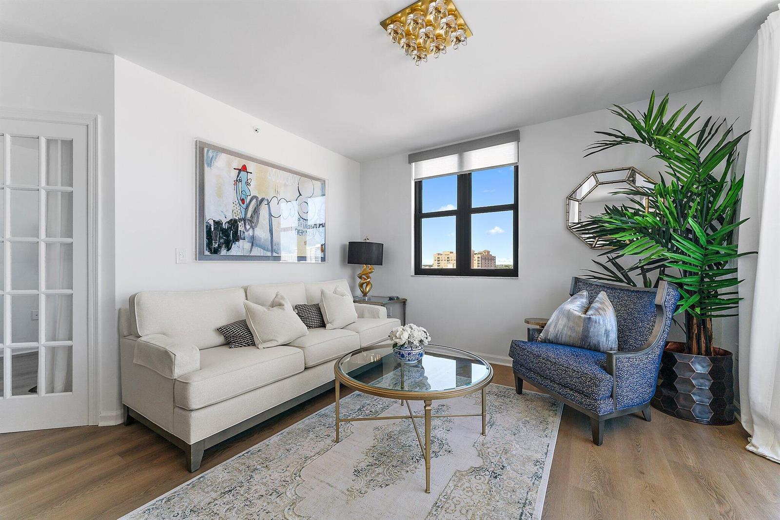 A living room features a beige sofa, blue armchair, glass coffee table, and large window — 651 Okeechobee Boulevard # 612, West Palm Beach FL 33401, WEST PALM BEACH, FL