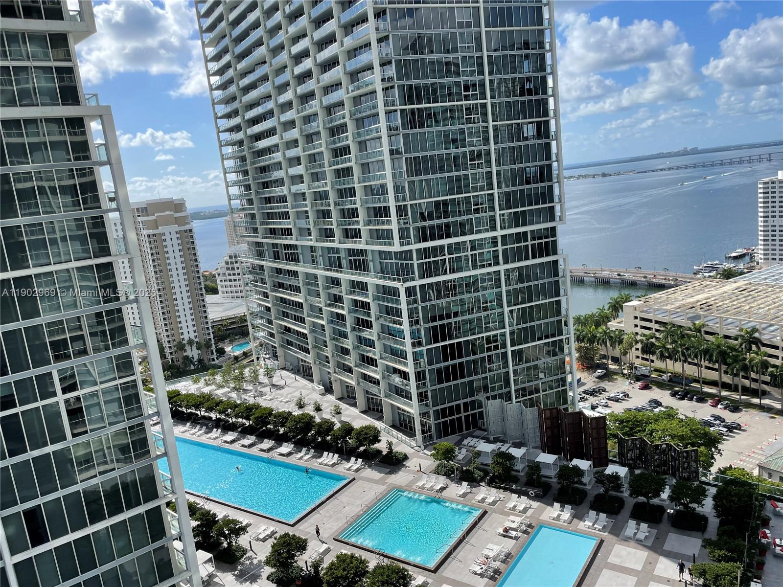 An elevated view shows multiple swimming pools on a terrace between two tall glass skyscrapers — 485 Brickell Ave # 2602, Miami FL 33131, MIAMI, FL