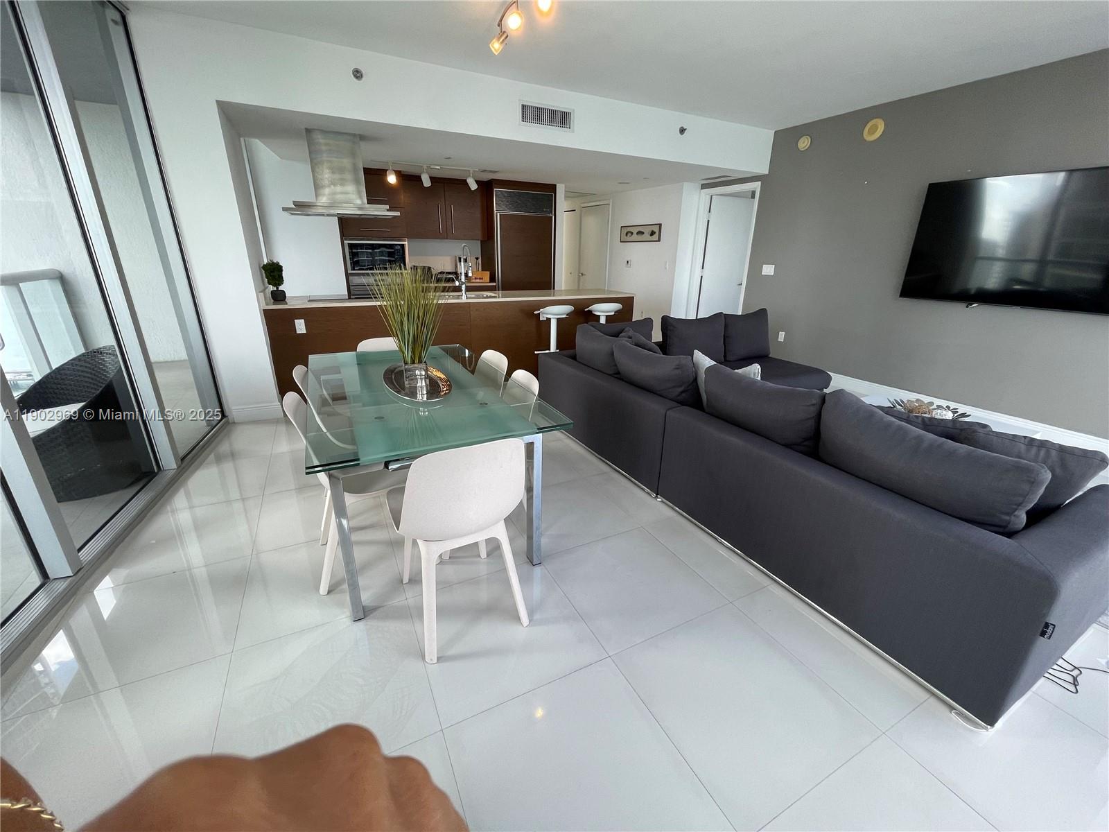An open-concept living and dining area features a glass table, dark sofa, and modern kitchen — 485 Brickell Ave # 2602, Miami FL 33131, MIAMI, FL