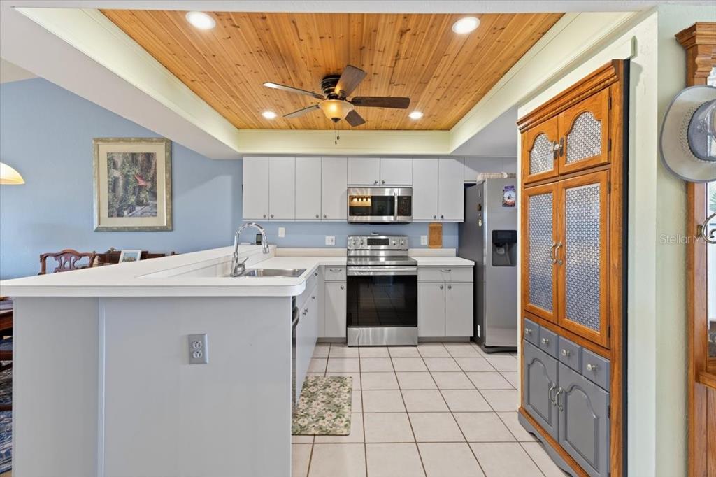 A kitchen features light gray cabinets, stainless steel appliances, and a wood-paneled tray ceiling — 6800 PLACIDA ROAD UNIT 2014, ENGLEWOOD, FL