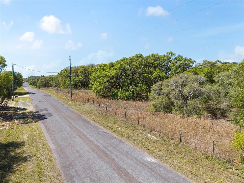 An asphalt road runs alongside a fenced, wooded lot under a blue sky — 5439 W OAKHILL STREET, DUNNELLON, FL