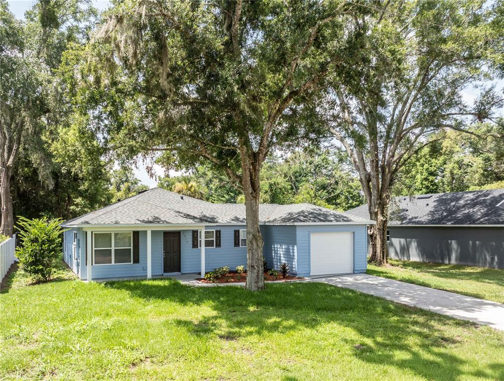 A light blue single-story house with a white garage door and a large front tree — 2270 SUANEE AVENUE, EUSTIS, FL
