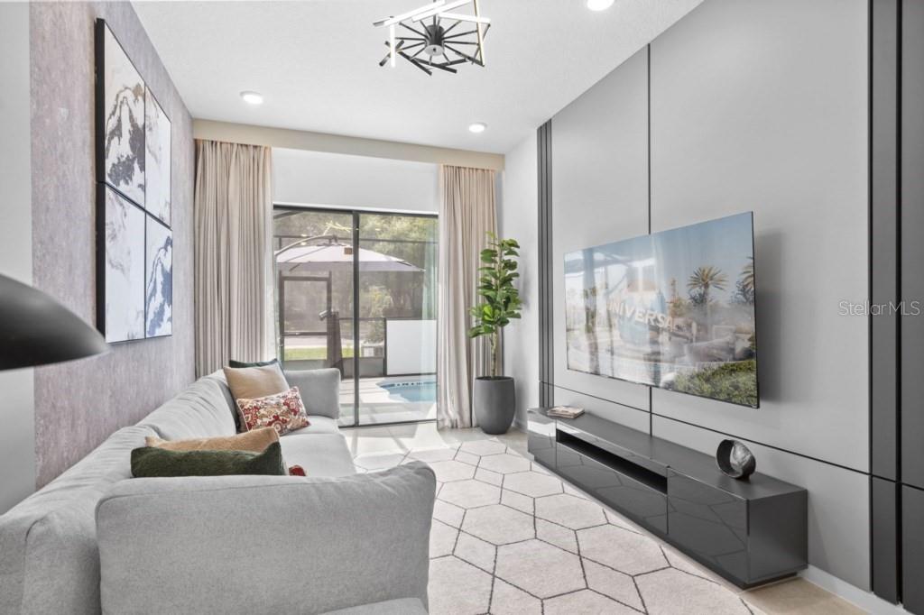 A modern living room features a gray sofa, a wall-mounted television, and a sliding glass door — 10424 EBB TIDE LANE, ORLANDO, FL