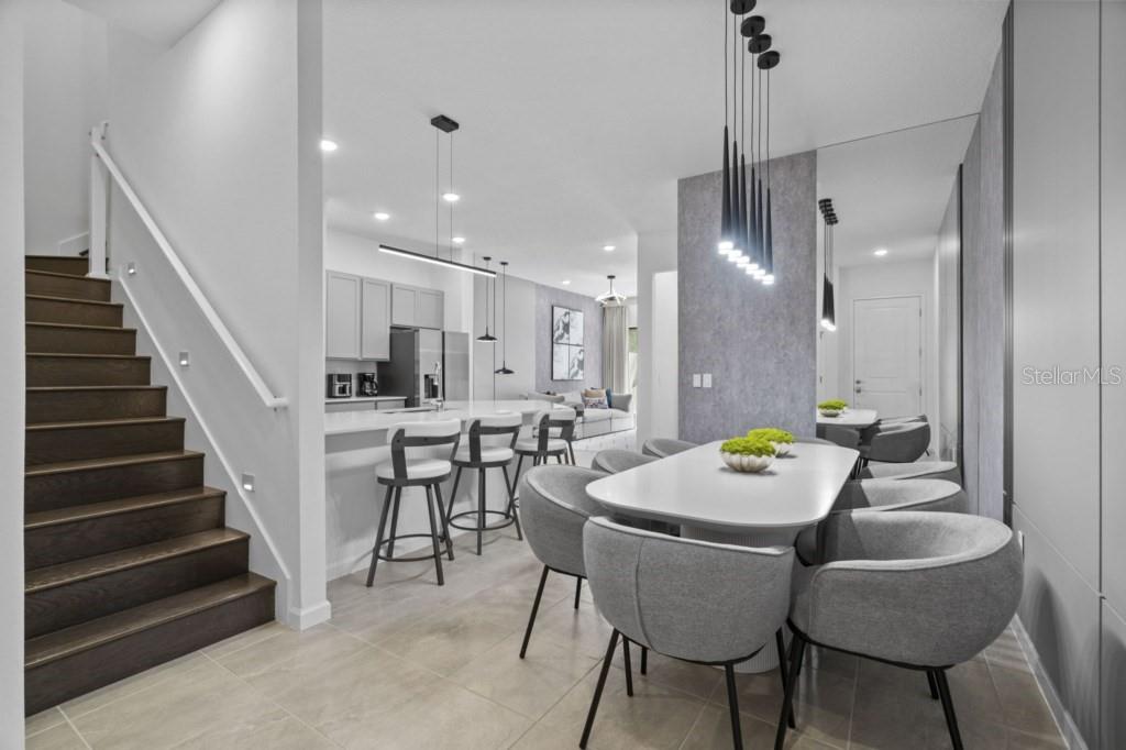 A modern open-concept dining area and kitchen featuring gray chairs, a white table, and stairs — 10424 EBB TIDE LANE, ORLANDO, FL