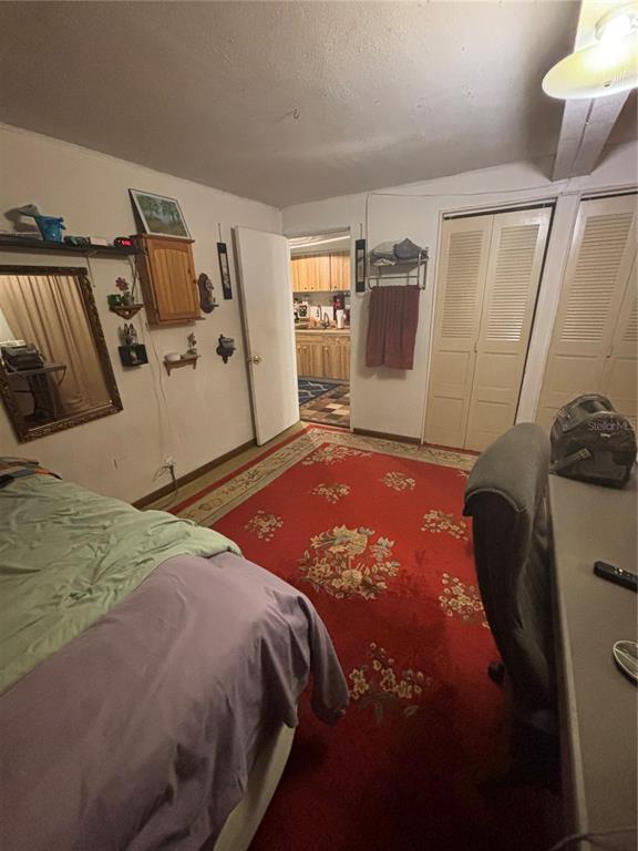 A bedroom with a red patterned rug, a bed, a desk, and a doorway to a kitchen — 1811 BEACHWAY LANE, ODESSA, FL