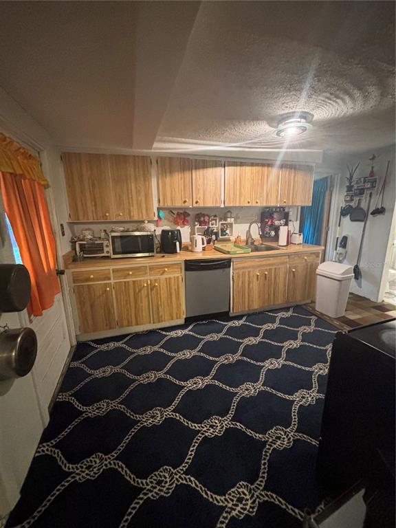 A kitchen features wood-grain cabinets, a dishwasher, and a blue rug with a rope pattern — 1811 BEACHWAY LANE, ODESSA, FL