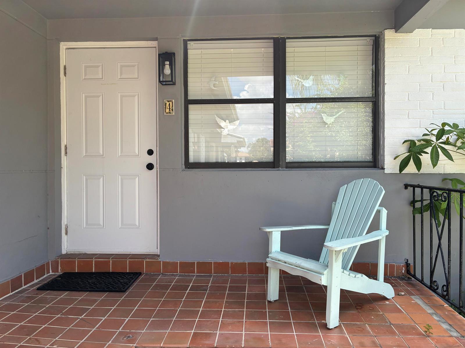 A light blue Adirondack chair sits on a tiled porch next to a white door — 130 S Lakeside Drive # 1, FL 33460, FL