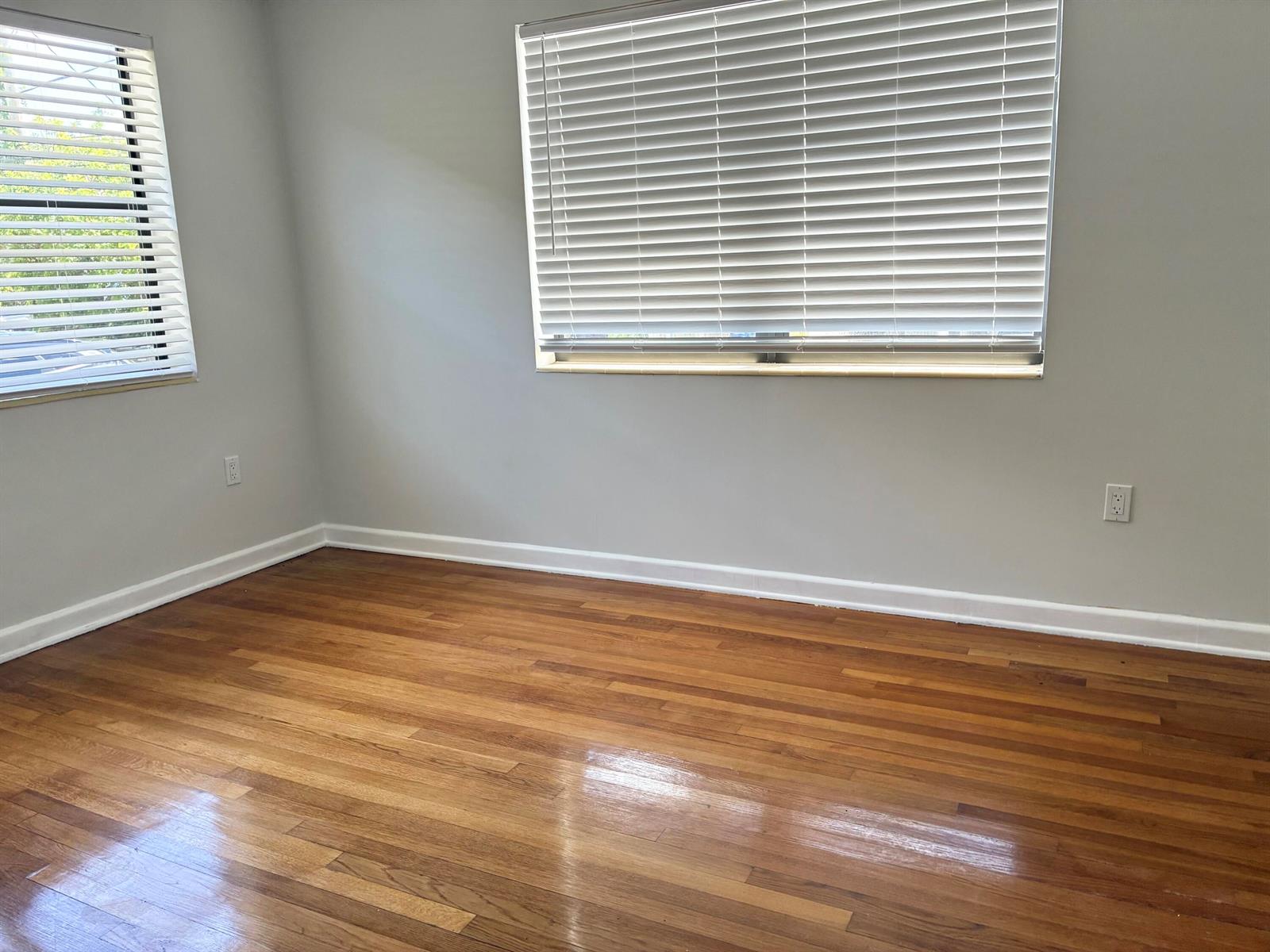 An empty room features hardwood floors, light gray walls, white trim, and two windowed walls — 130 S Lakeside Drive # 1, FL 33460, FL