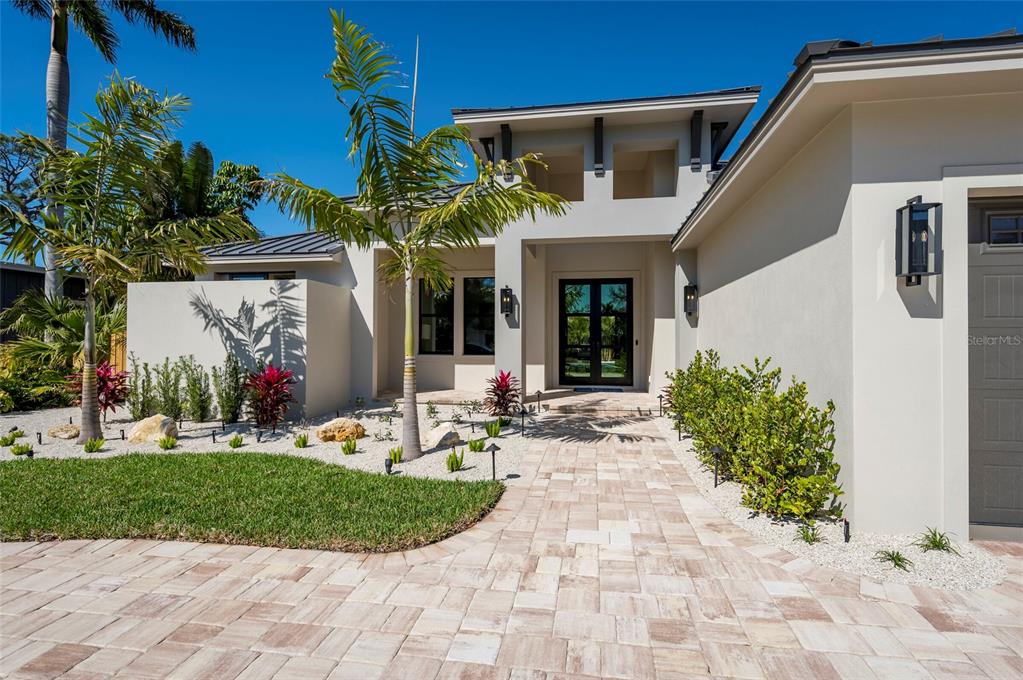A modern house exterior features a paved walkway, palm trees, and a glass-paneled front door — 1959 WISTERIA STREET, SARASOTA, FL