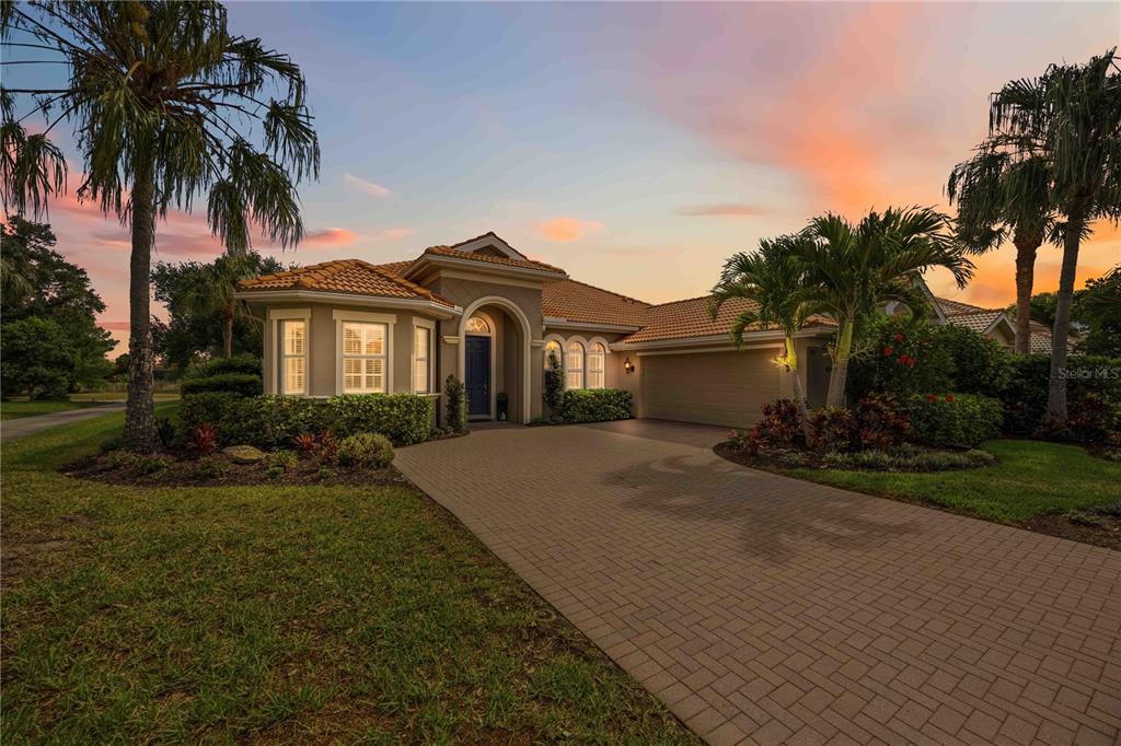 A single-story house with a tiled roof, arched entryway, and paved driveway at sunset — 170 MONTELLUNA DRIVE, NORTH VENICE, FL