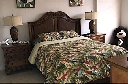 A bedroom features a wooden bed frame, tropical-patterned bedding, two matching nightstands with lamps, and a stuffed animal — 6917 Collins Ave, Miami Beach FL 33141, MIAMI BEACH, FL