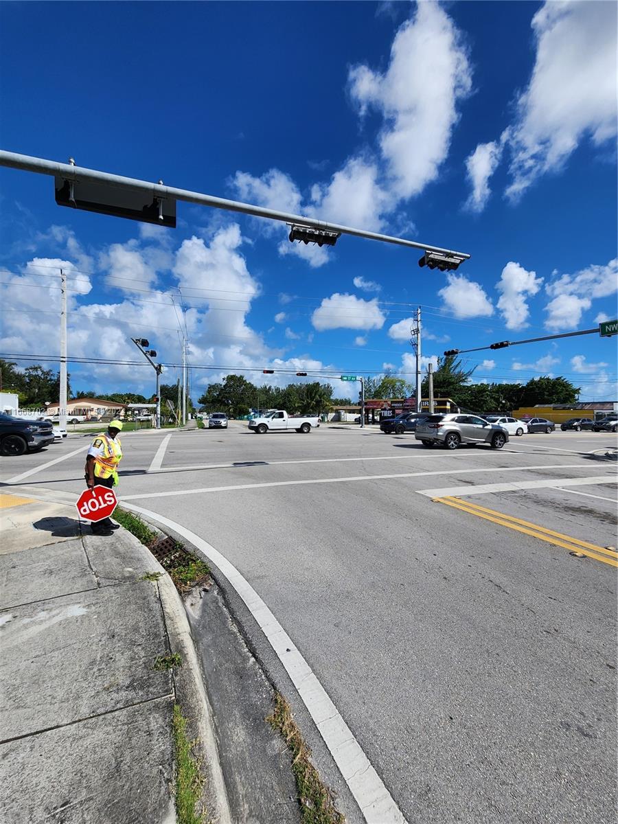 A crossing guard stands at a sunny intersection with traffic lights and multiple vehicles — 11110/20 NW 17th Ave, Miami FL 33167, MIAMI, FL