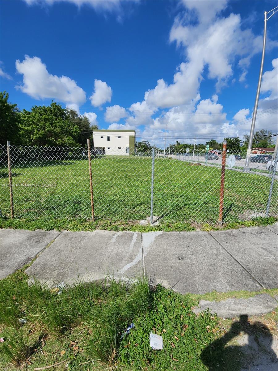 A chain-link fence encloses a vacant, grassy lot under a blue sky with clouds — 11110/20 NW 17th Ave, Miami FL 33167, MIAMI, FL