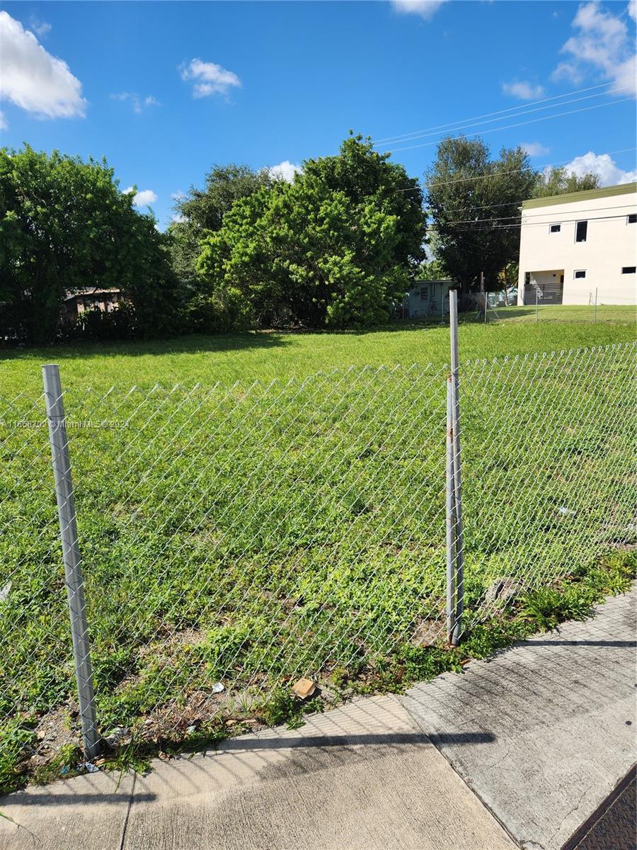 A chain-link fence encloses a grassy vacant lot with trees and a building in the background — 11110/20 NW 17th Ave, Miami FL 33167, MIAMI, FL