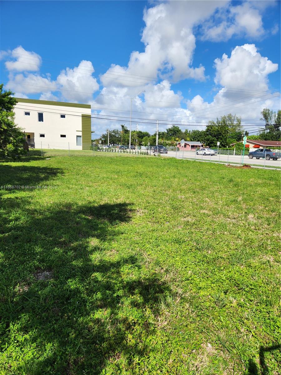 A vacant, grassy lot sits adjacent to a modern multi-story building and a paved road — 11110/20 NW 17th Ave, Miami FL 33167, MIAMI, FL