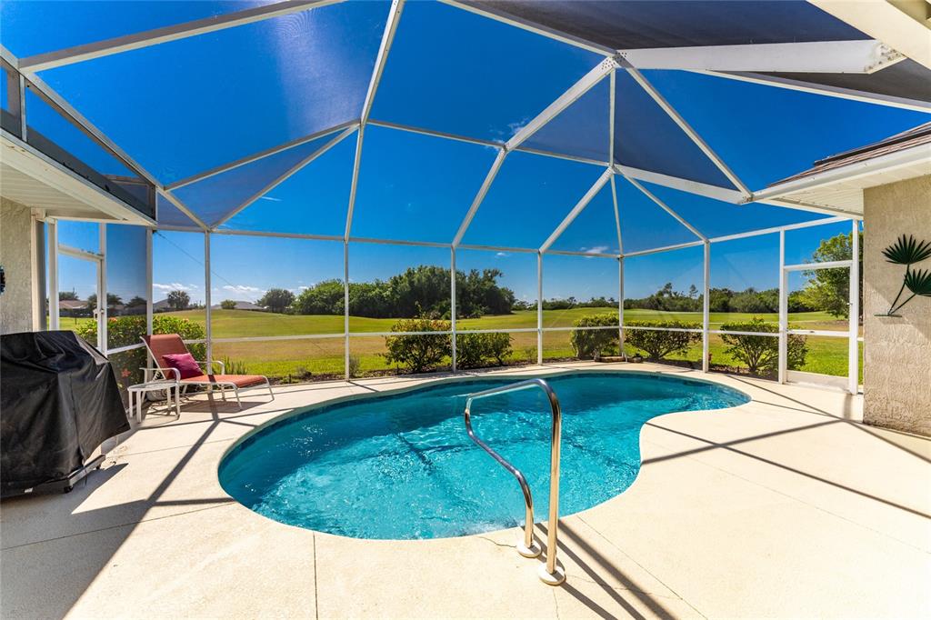 A screened-in pool patio overlooks a golf course under a clear blue sky — 28 MEDALIST COURT, ROTONDA WEST, FL