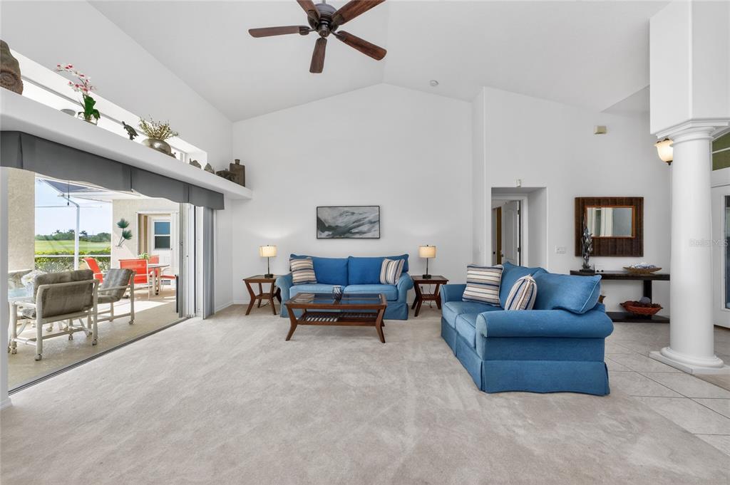 A living room with blue sofas, carpeted floors, and a sliding door to a patio — 28 MEDALIST COURT, ROTONDA WEST, FL
