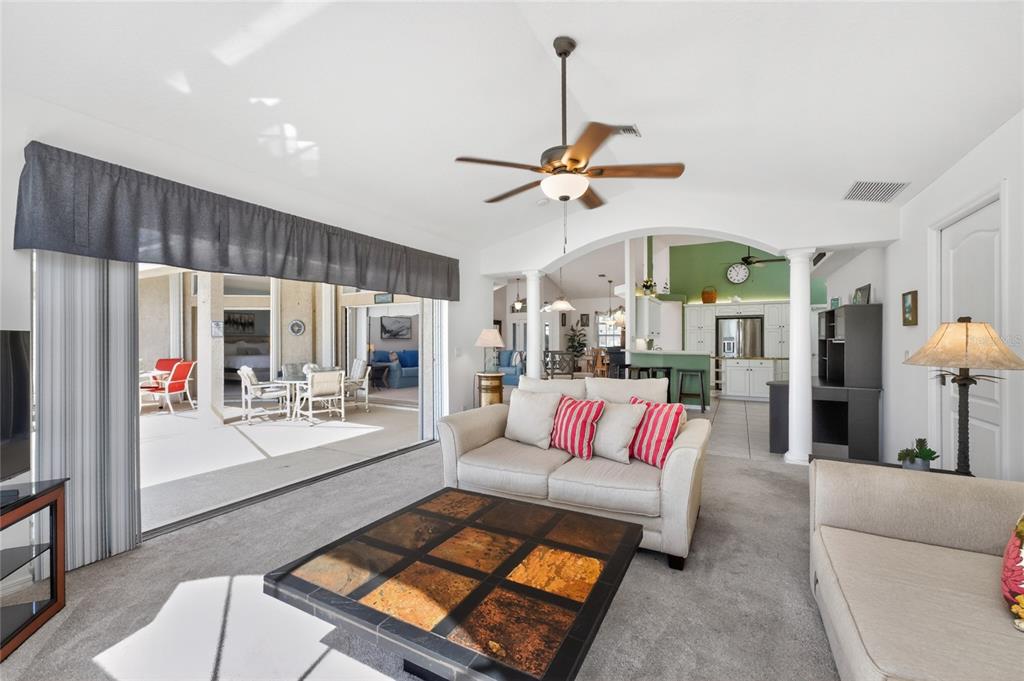 A living room with carpeted floors, a slate coffee table, and an open kitchen view — 28 MEDALIST COURT, ROTONDA WEST, FL