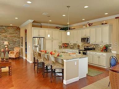 A kitchen with white cabinets, a granite-topped island, and hardwood floors opens to a living area — 2810 SWOOP CIRCLE, KISSIMMEE, FL