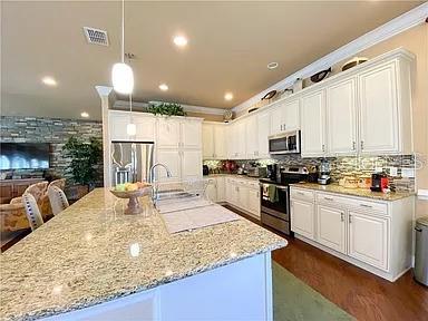 A kitchen features white cabinetry, granite countertops, a large island, and stainless steel appliances — 2810 SWOOP CIRCLE, KISSIMMEE, FL