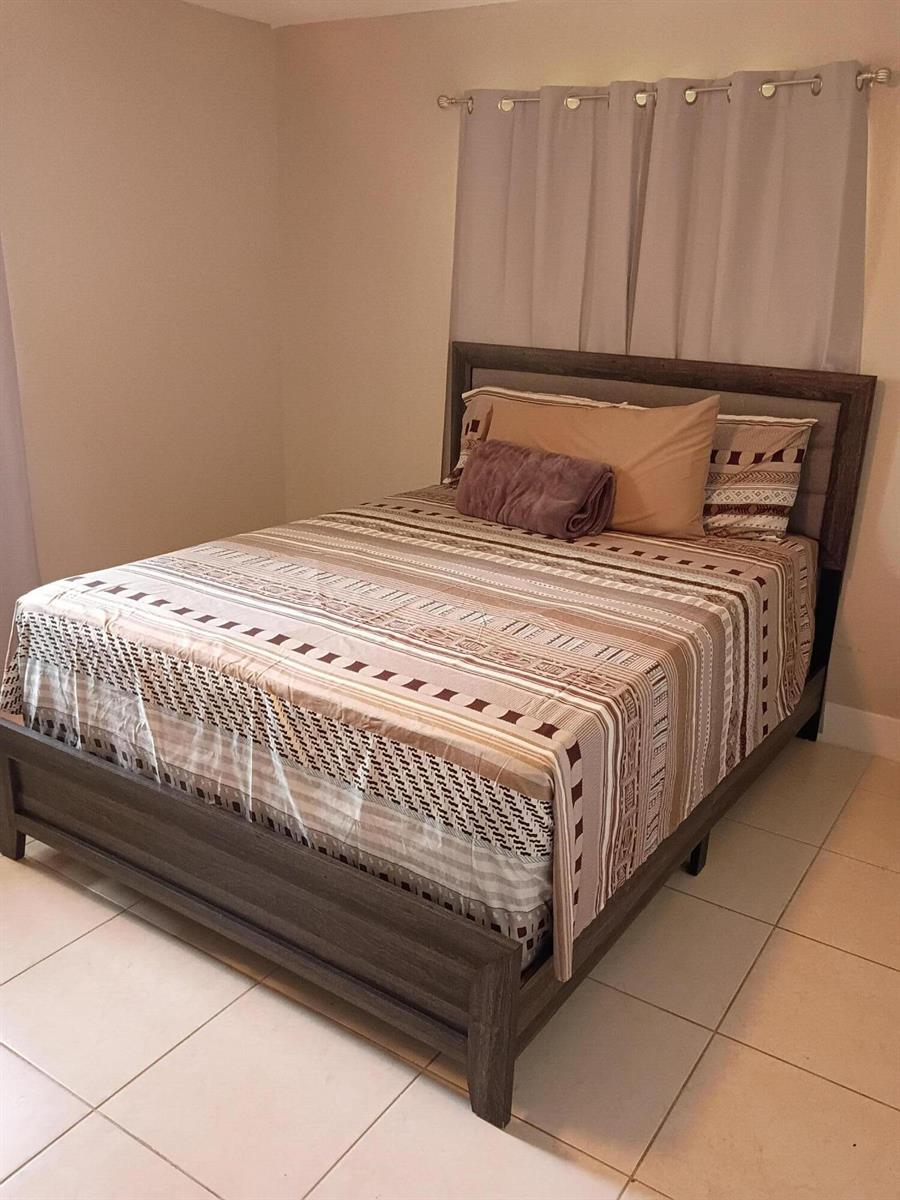 A bedroom features a wooden bed frame with striped bedding against a light-colored wall — 1270 NW 66th Terrace, Margate FL 33063, MARGATE, FL