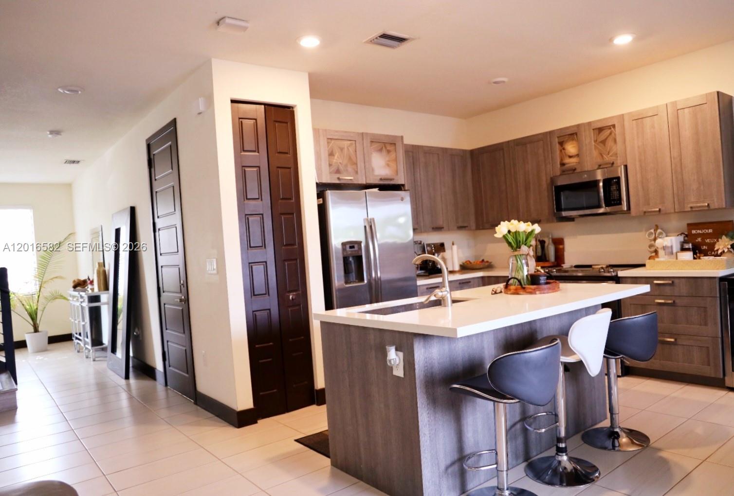 A modern kitchen features gray cabinetry, a white quartz island, and stainless steel appliances — 16012 NW 91st Ct, Miami Lakes FL 33018, MIAMI LAKES, FL