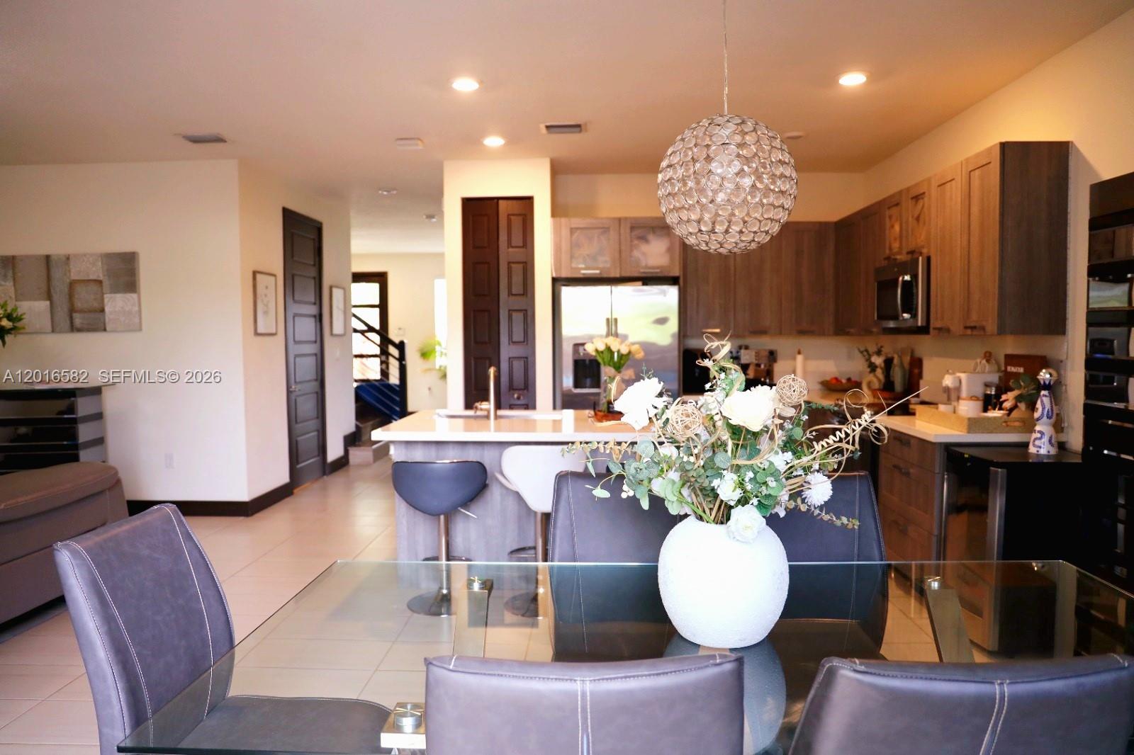 A living and dining area features a grey sectional sofa, glass table, and modern lighting — 16012 NW 91st Ct, Miami Lakes FL 33018, MIAMI LAKES, FL
