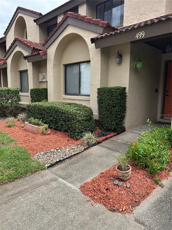 The exterior of a tan stucco townhouse features arched windows, red tile roofing, and landscaping — 499 CLUB DRIVE, WINTER SPRINGS, FL