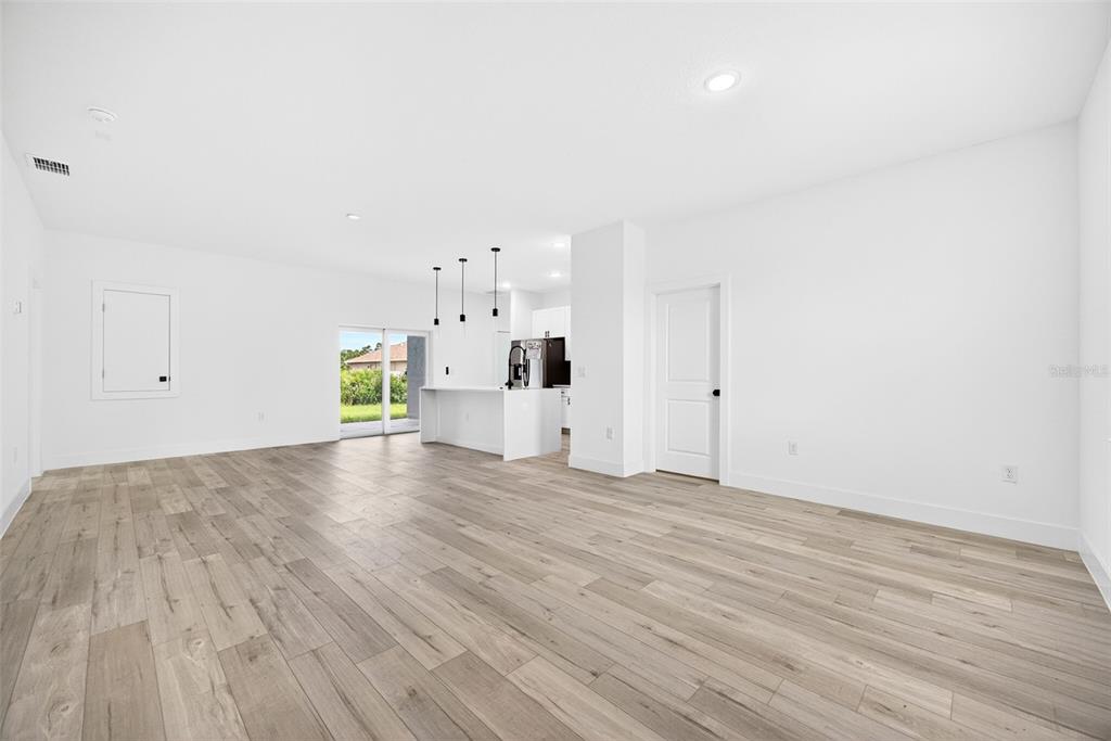 An open-concept living area with light wood-look flooring, white walls, and a kitchen island — 6223 EMMONSDALE STREET, PORT CHARLOTTE, FL