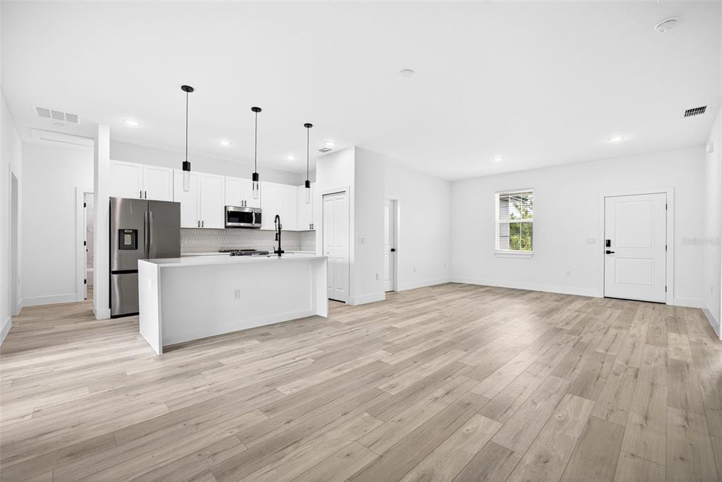 A modern kitchen with white cabinets and an island opens into a spacious living area — 6223 EMMONSDALE STREET, PORT CHARLOTTE, FL
