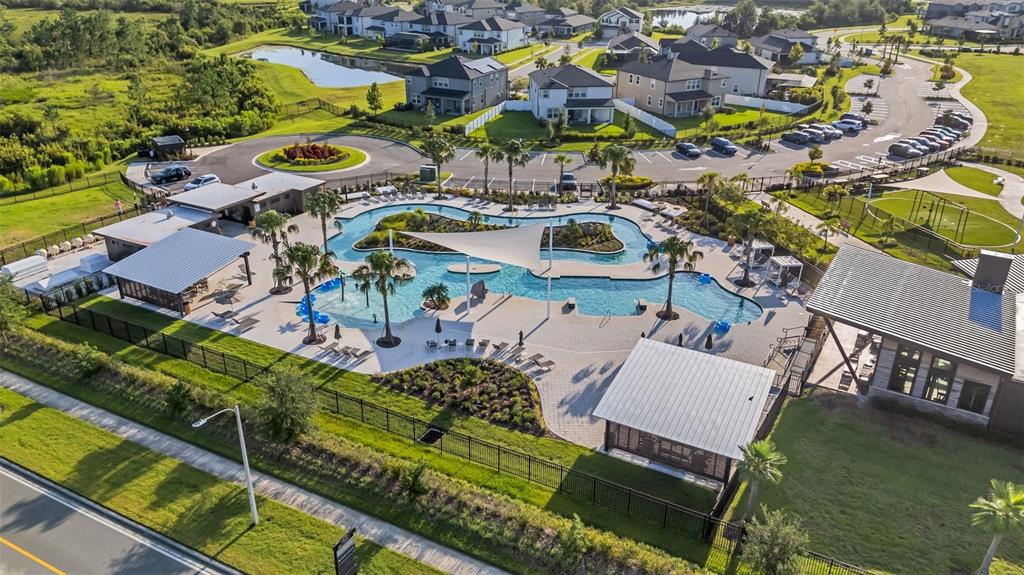 An aerial view shows a community swimming pool with a lazy river and lounge areas — 5841 RIVERSTON AVENUE, WESLEY CHAPEL, FL