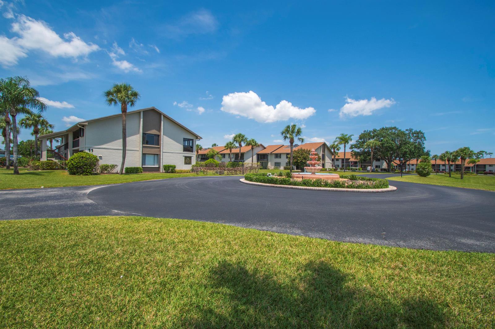 A circular driveway with a central fountain leads to multi-story apartment buildings and palm trees — 1600 NE Dixie Highway # 103, Jensen Beach FL 34957, JENSEN BEACH, FL