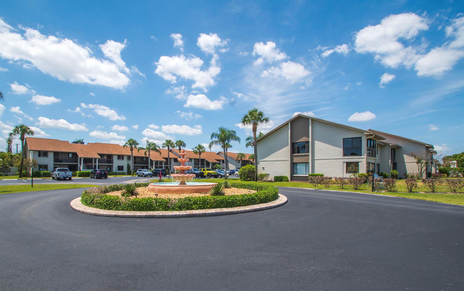 A multi-story apartment complex features a central fountain in a circular driveway with palm trees — 1600 NE Dixie Highway # 103, Jensen Beach FL 34957, JENSEN BEACH, FL