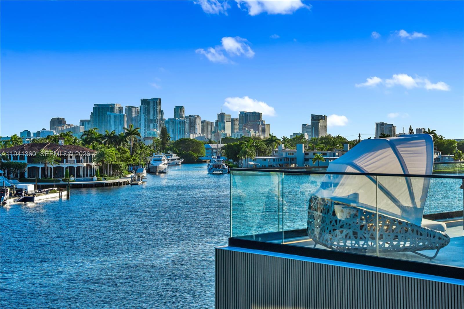 A balcony with a lounge chair overlooks a canal and a distant city skyline — 725 Middle River Dr, Fort Lauderdale FL 33304, FORT LAUDERDALE, FL