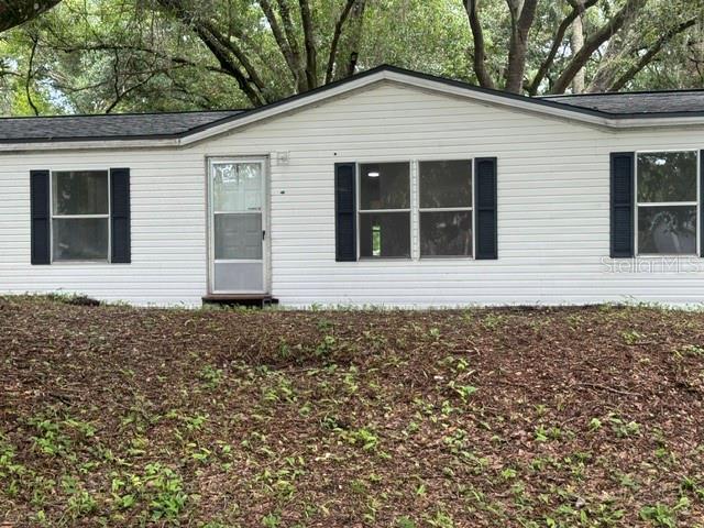 A single-story white mobile home with dark shutters sits in a yard with trees — 6633 GLEN MEADOW LOOP, LAKELAND, FL