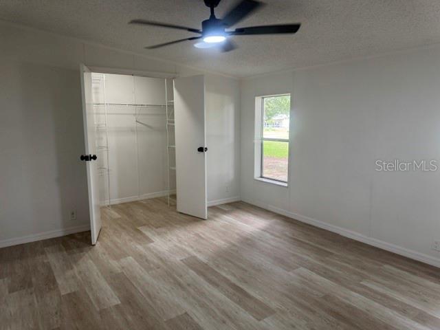 A bedroom with light wood-look flooring, a ceiling fan, and an open white closet — 6633 GLEN MEADOW LOOP, LAKELAND, FL