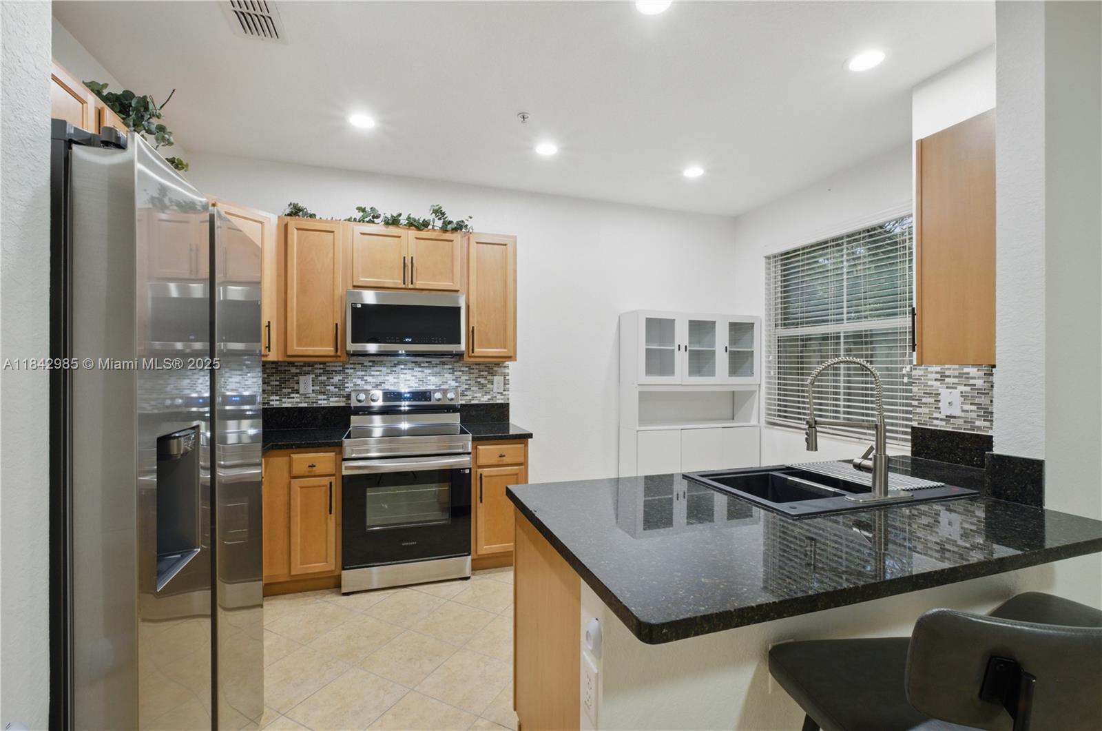 A kitchen features light wood cabinets, black granite countertops, stainless steel appliances, and tile flooring — 2851 W Prospect Rd # 307, Tamarac FL 33309, TAMARAC, FL