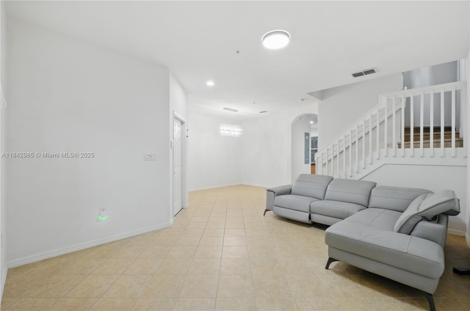 A living room features light-colored tile flooring, white walls, and a gray sectional sofa — 2851 W Prospect Rd # 307, Tamarac FL 33309, TAMARAC, FL