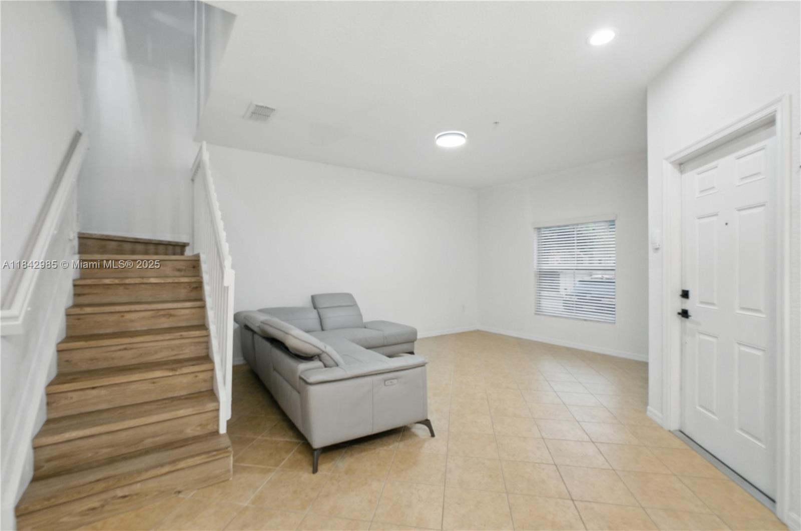 A living room features a gray sectional sofa, tile flooring, and a wooden staircase — 2851 W Prospect Rd # 307, Tamarac FL 33309, TAMARAC, FL