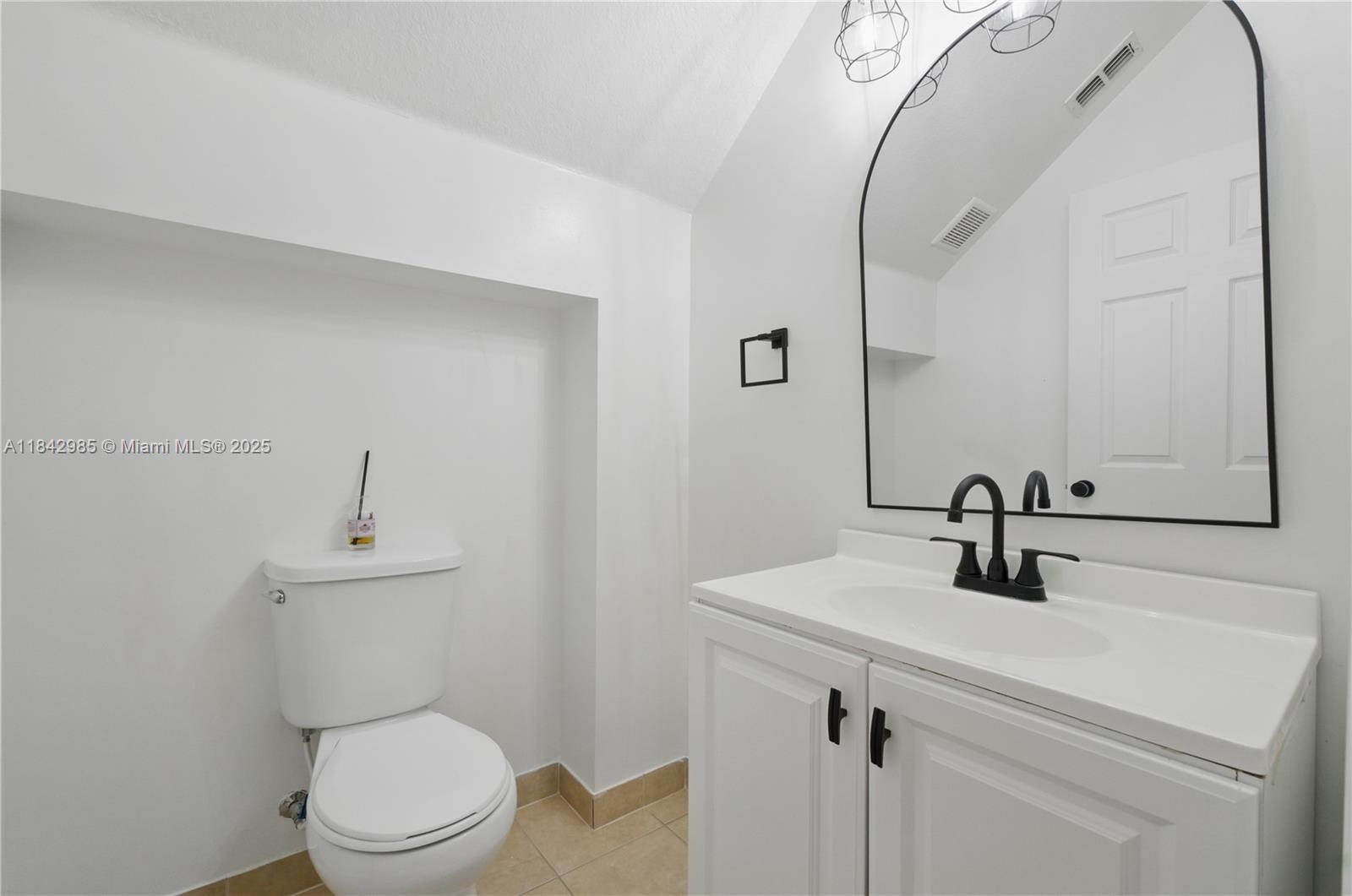 This bathroom features a white vanity with a black faucet, a toilet, and an arched mirror — 2851 W Prospect Rd # 307, Tamarac FL 33309, TAMARAC, FL