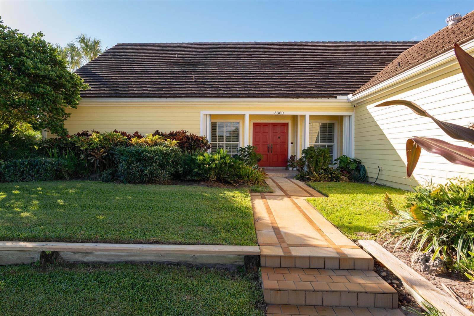 The exterior of a yellow house features a red double front door and a walkway — 3360 SE Golf Trail, Stuart FL 34997, STUART, FL
