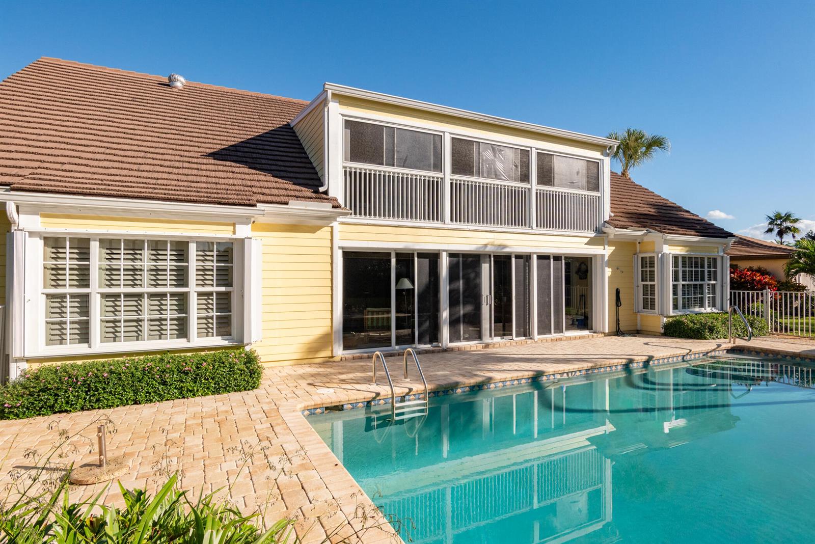 A yellow house with a screened-in porch, garage, and concrete driveway under a blue sky — 3360 SE Golf Trail, Stuart FL 34997, STUART, FL