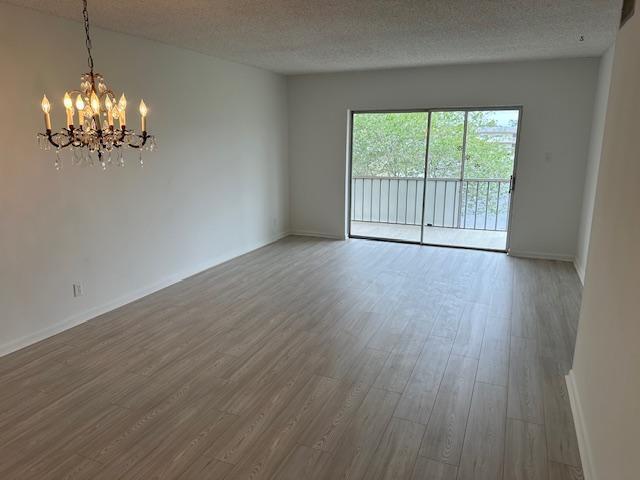 An empty living room with light wood-look flooring, a crystal chandelier, and a sliding glass door — 7805 W Atlantic Boulevard # 202, Margate FL 33063, MARGATE, FL