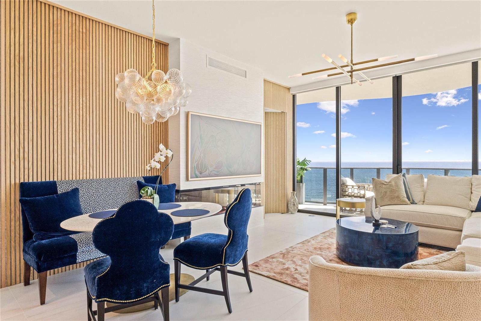 A modern living and dining area features wood-slatted walls, blue velvet furniture, and ocean views — 900 N Ocean Boulevard, Pompano Beach FL 33062, POMPANO BEACH, FL