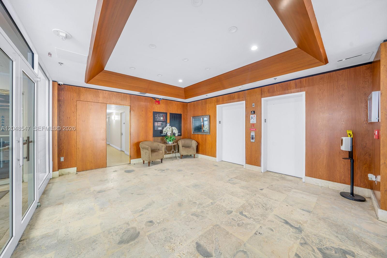 This lobby features wood-paneled walls, two elevators, tile flooring, and a recessed ceiling design — 2400 SW 3rd Ave # 706, Miami FL 33129, MIAMI, FL