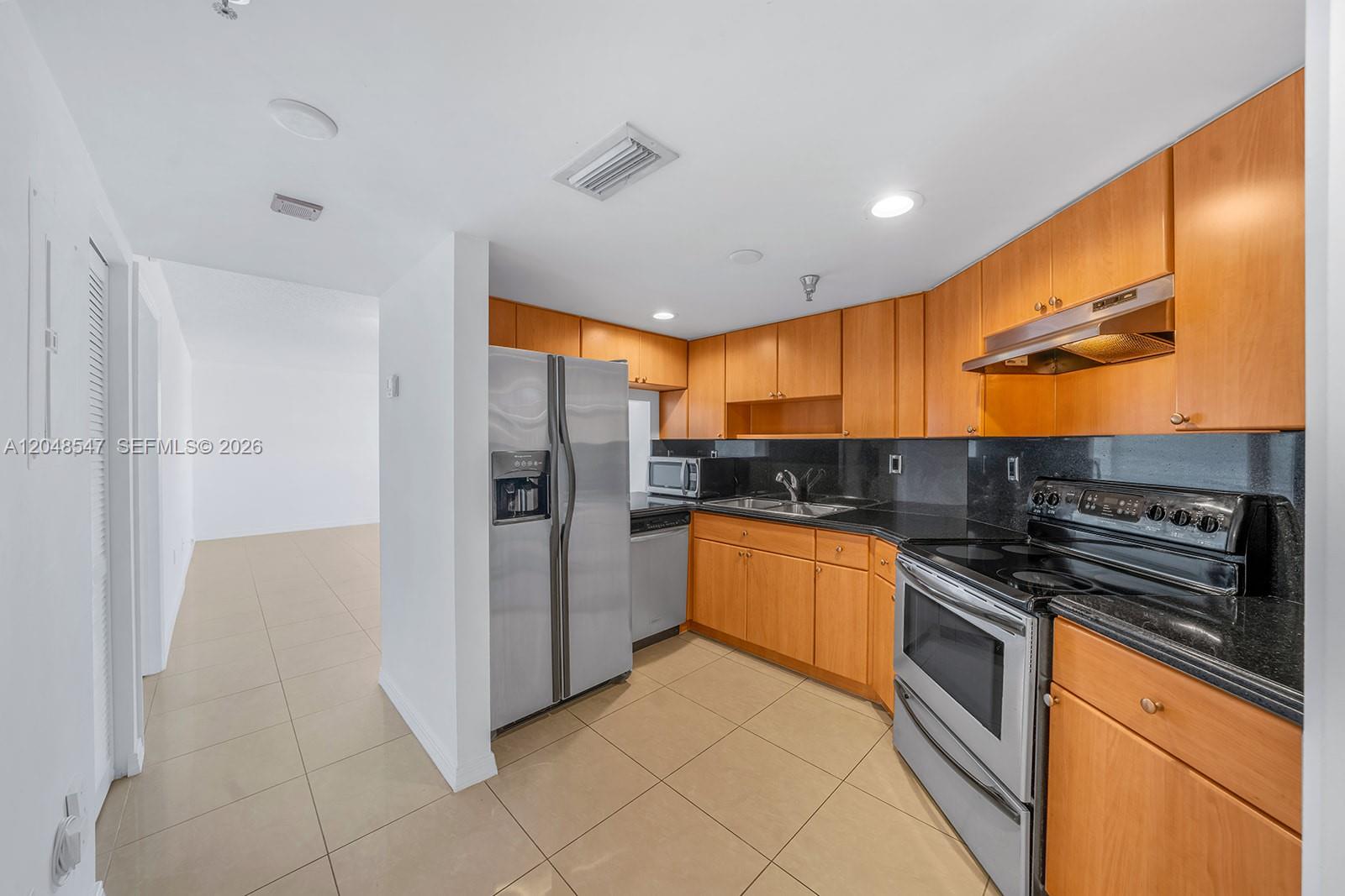 A kitchen features wood cabinets, black countertops, stainless steel appliances, and light tile flooring — 2400 SW 3rd Ave # 706, Miami FL 33129, MIAMI, FL